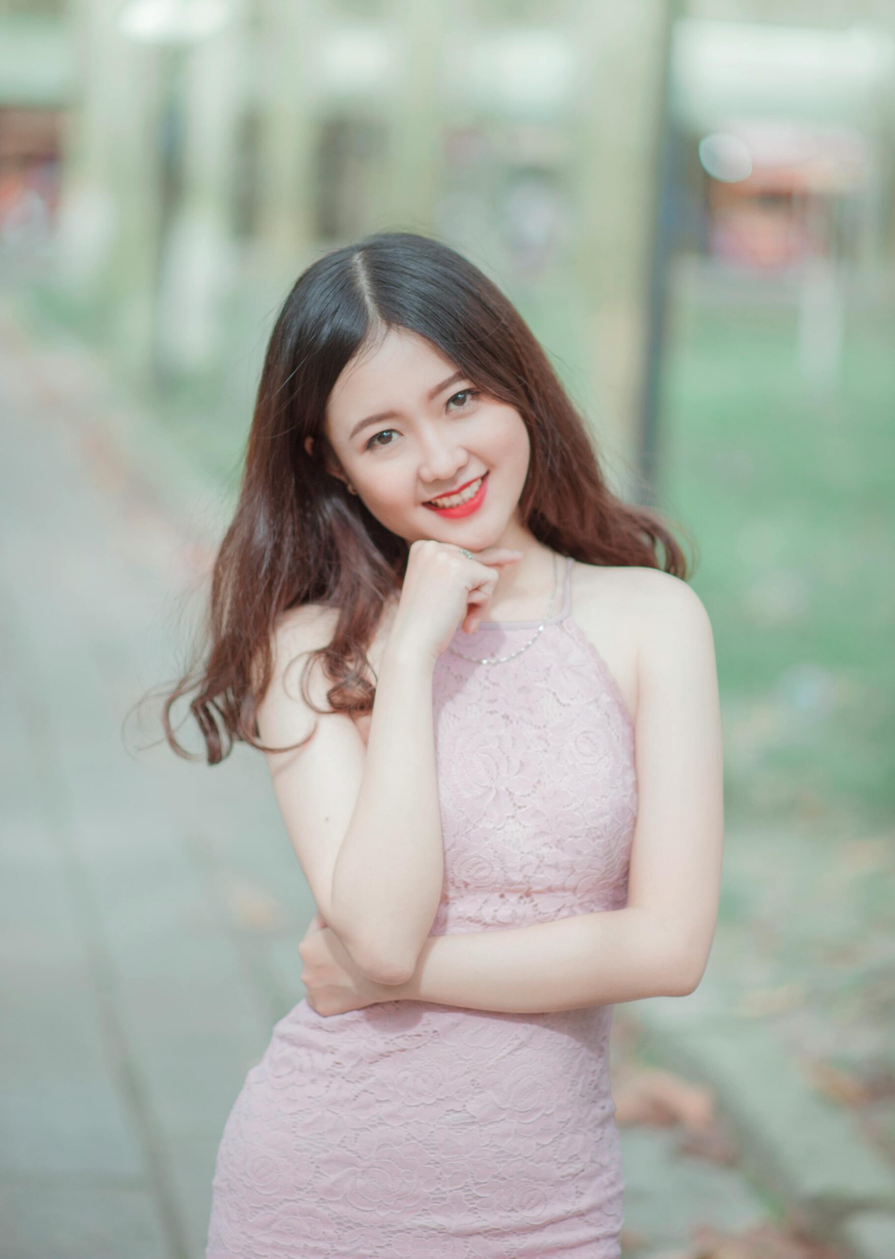 Young woman posing outdoors with a confident smile in an elegant pink dress.